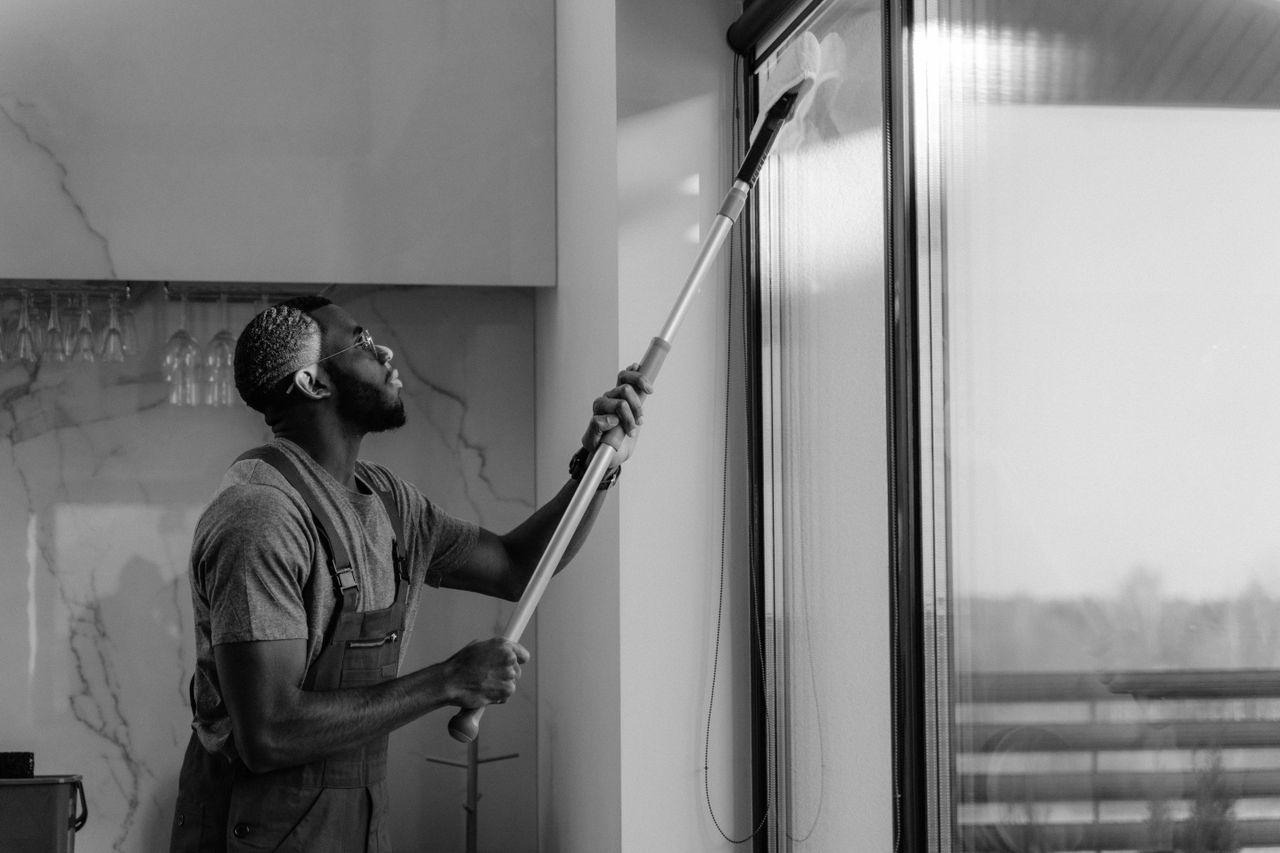 A man cleaning a glass window with a mop in grayscale, showcasing professional work.